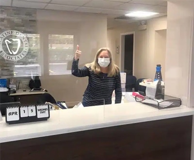 Dental receptionist wearing mask at front desk in modern dental office reception area.