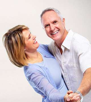 Middle-aged couple smiling and embracing against white background in dental office setting.