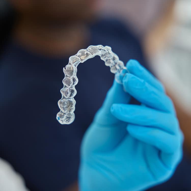Gloved hand holding clear dental aligner or retainer against blurred background