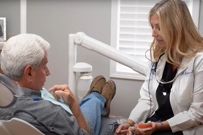 Female dentist discussing treatment with senior male patient in dental office chair.