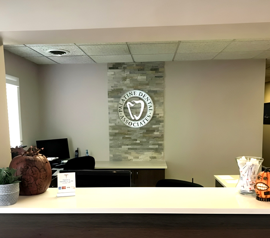 Reception desk at Palatine Dental Associates with staff member, modern office interior, and logo signage.