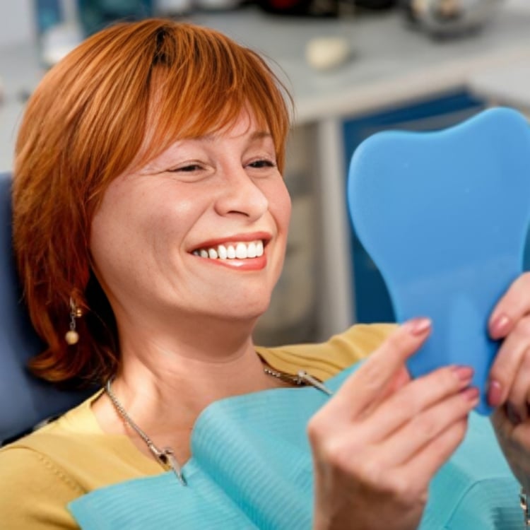 Smiling woman holding blue dental model in modern dental office setting.