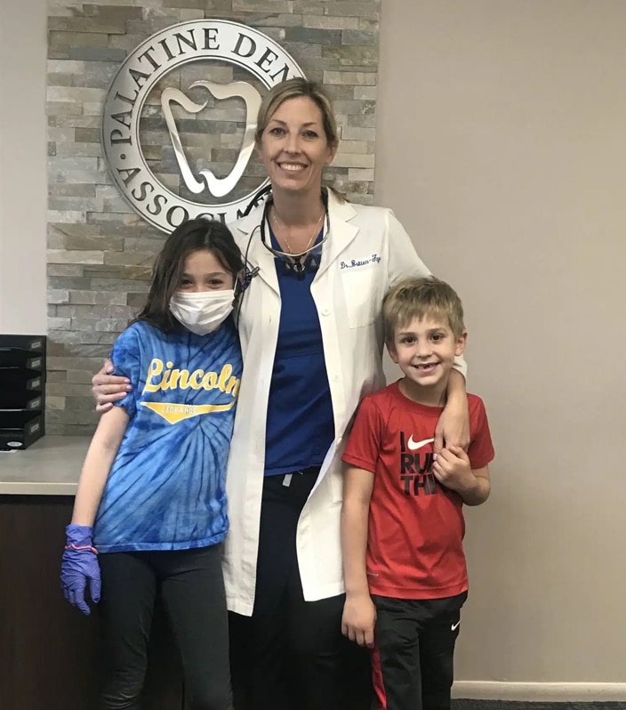 Female dentist with two children in dental office, all smiling at camera.