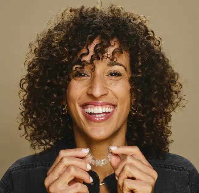 Smiling woman with curly dark hair holding dental floss against neutral background