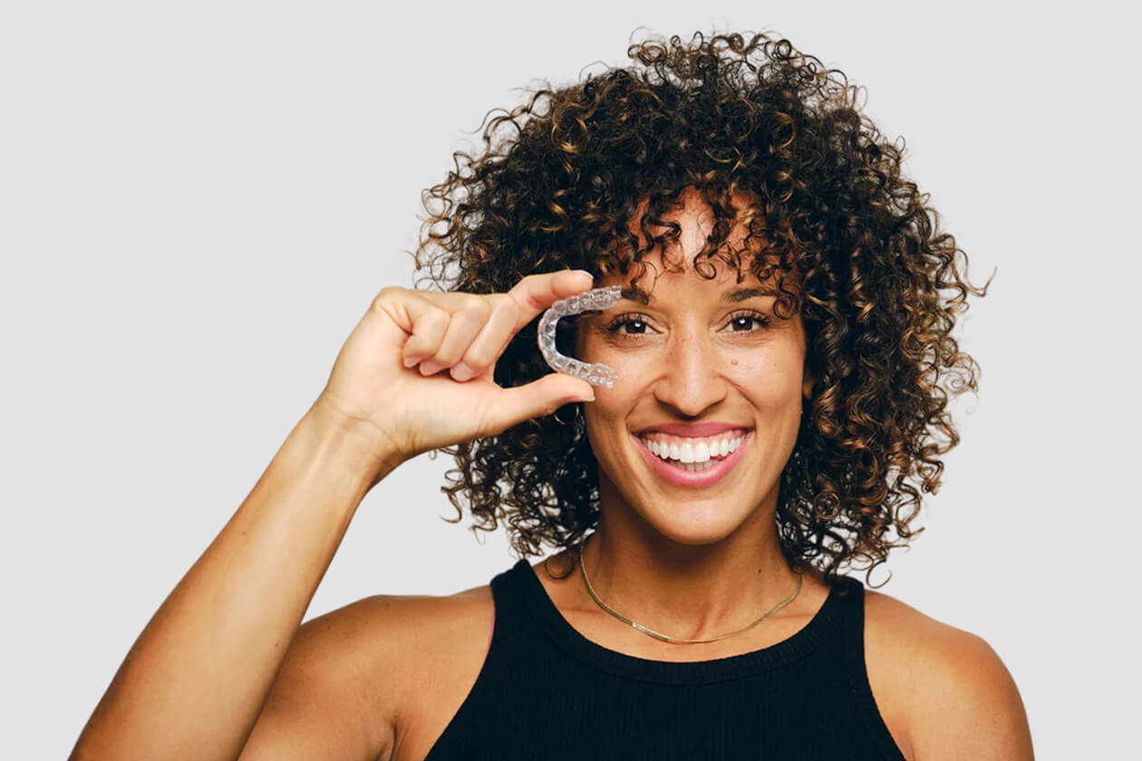 Smiling woman with curly hair making phone gesture against white background.