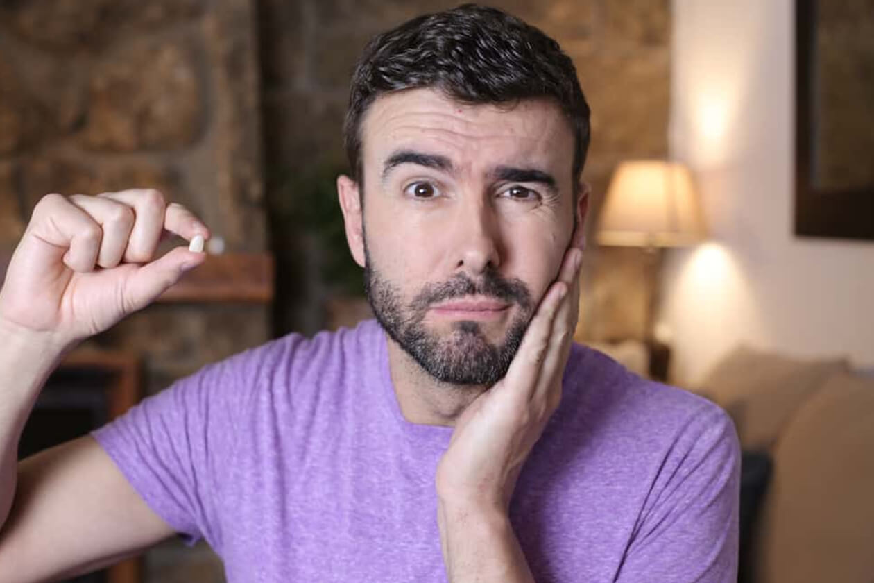 Man in purple shirt touching face with concerned expression in home interior setting