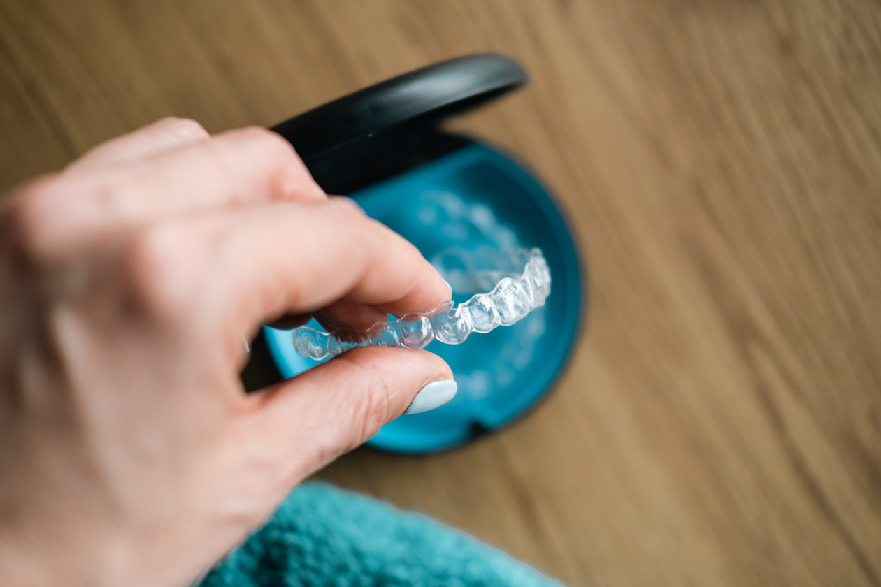 Hand holding blue dental mirror showing white teeth during oral examination on wooden surface.