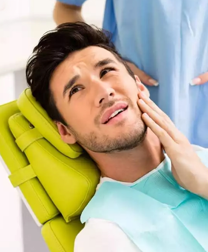 Man experiencing tooth pain in dental office setting, holding cheek.