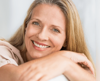Woman smiling warmly at camera with arms crossed in professional dental office portrait
