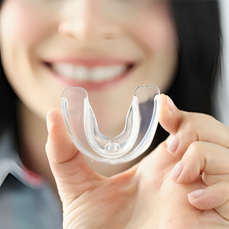 Woman smiling while holding clear dental retainer or aligner in her hand.