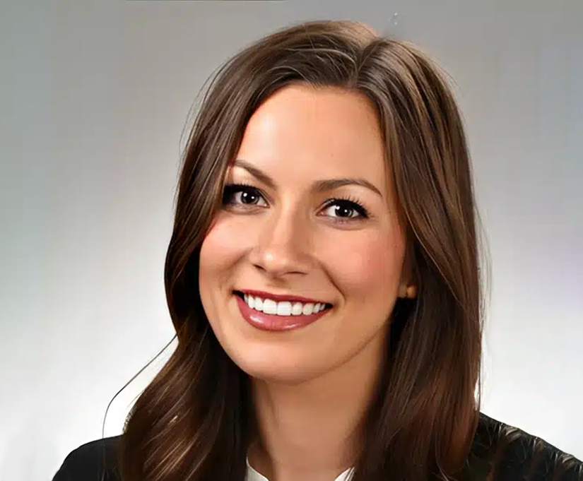 Professional headshot of smiling woman with long brown hair in business attire against neutral background.