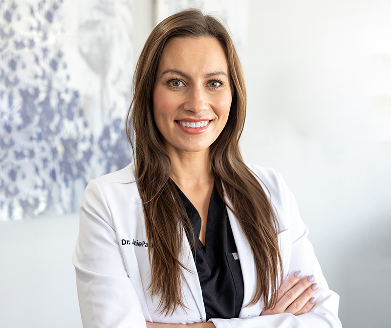 Professional female dentist in white coat smiling at camera in modern dental office setting.