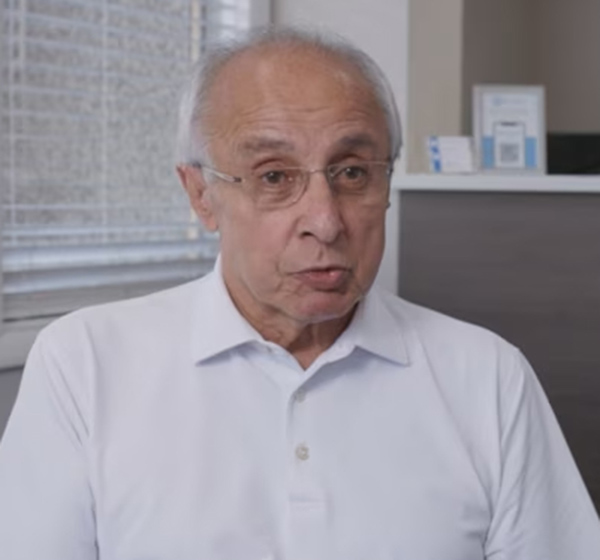 Senior man wearing glasses and light blue shirt in dental office setting.
