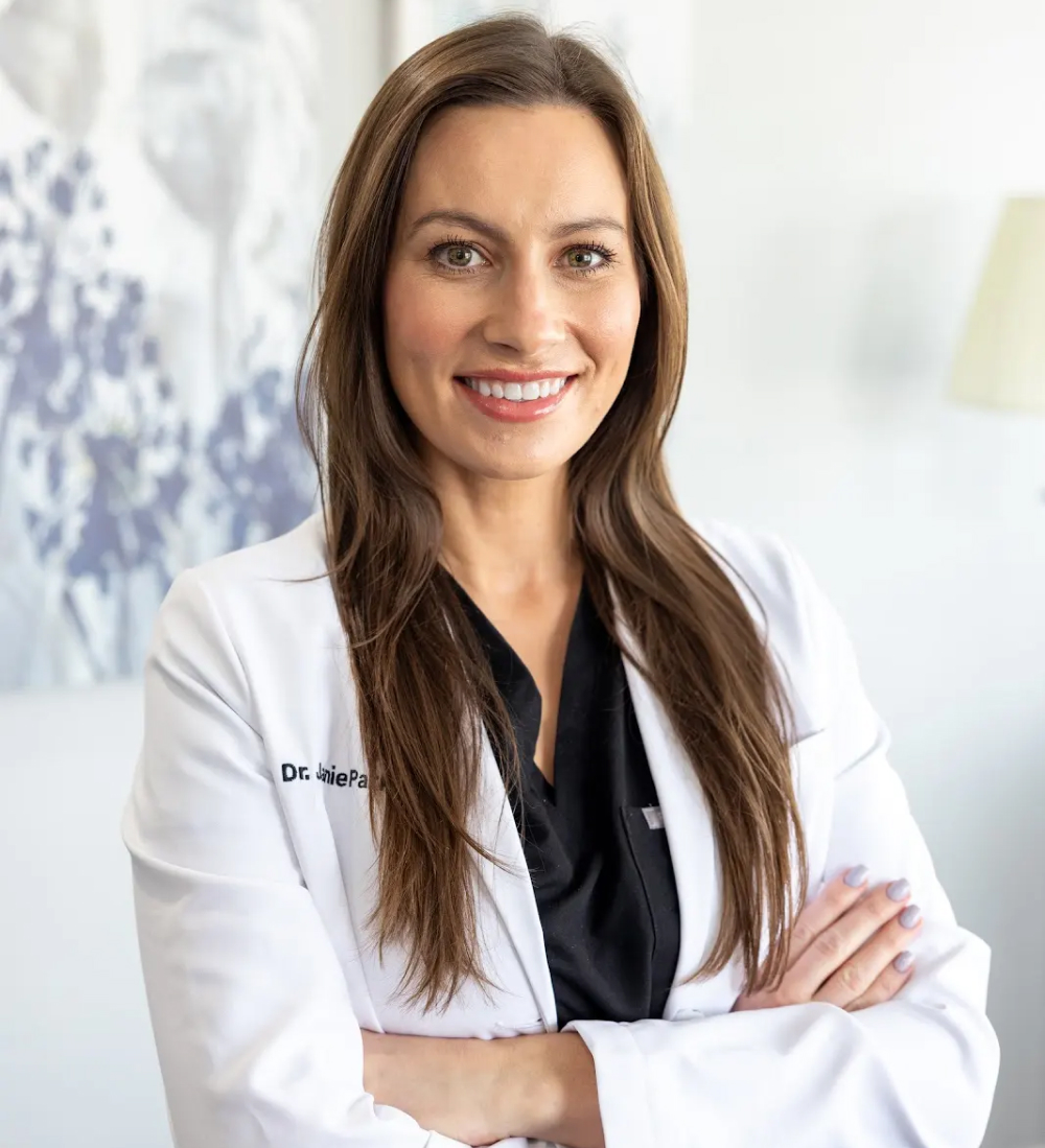 Female dentist in white coat smiling with arms crossed in professional dental office setting.