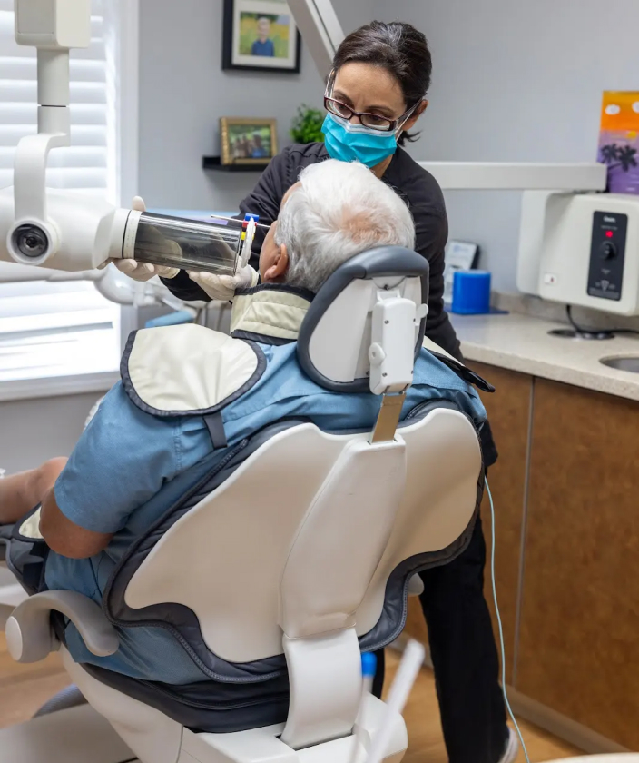 Dentist in mask examines patient in dental chair at Palatine Dental Associates office.