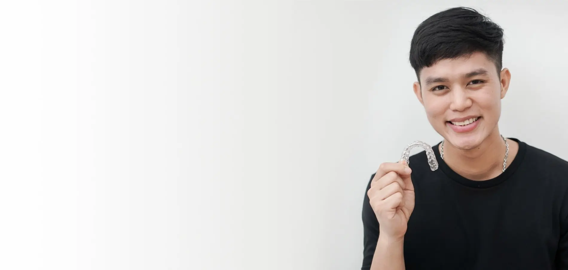 Young man in black shirt smiling and holding dental floss against white background.
