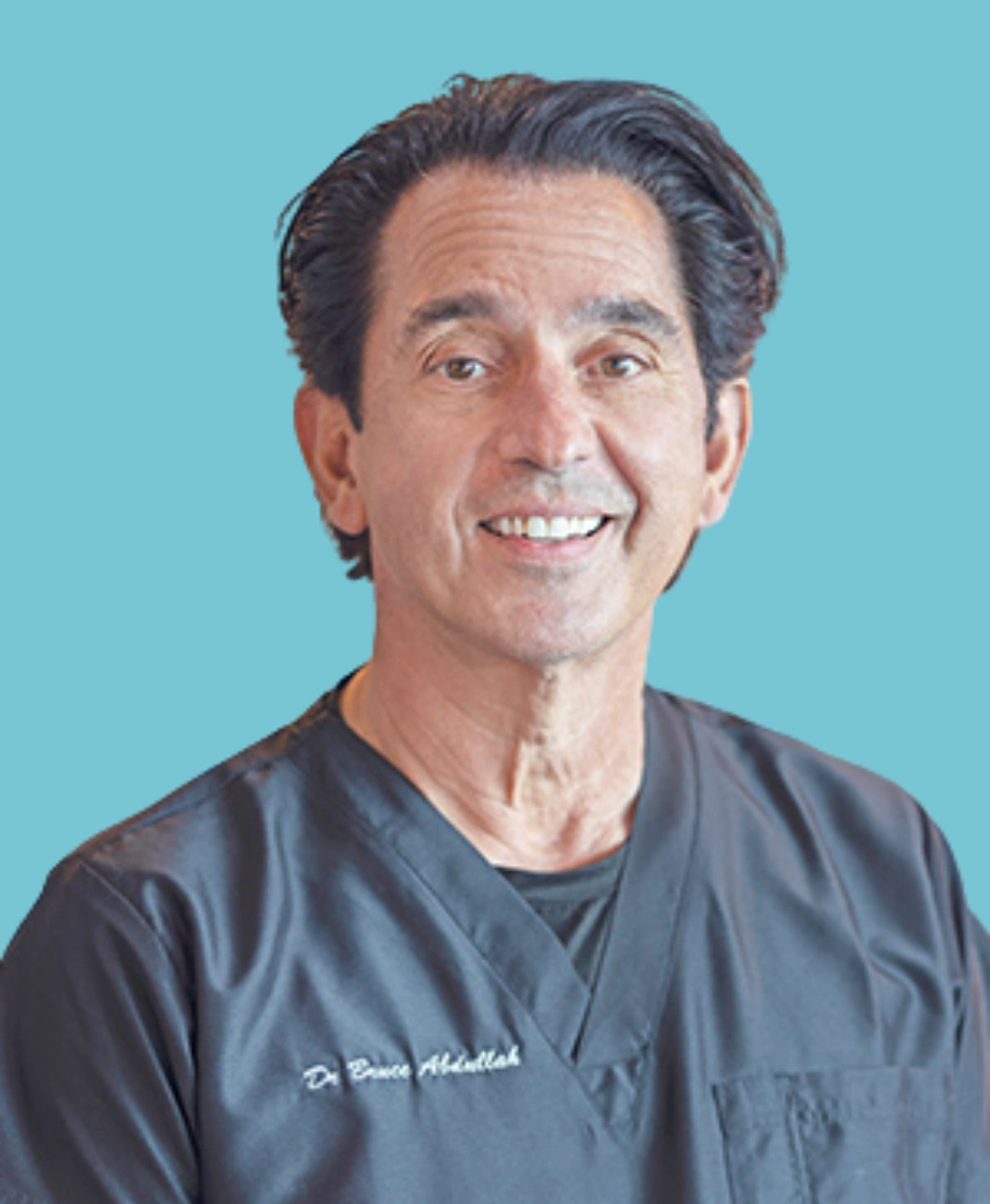 Male dentist wearing blue scrubs smiling against blue background, Palatine Dental Associates