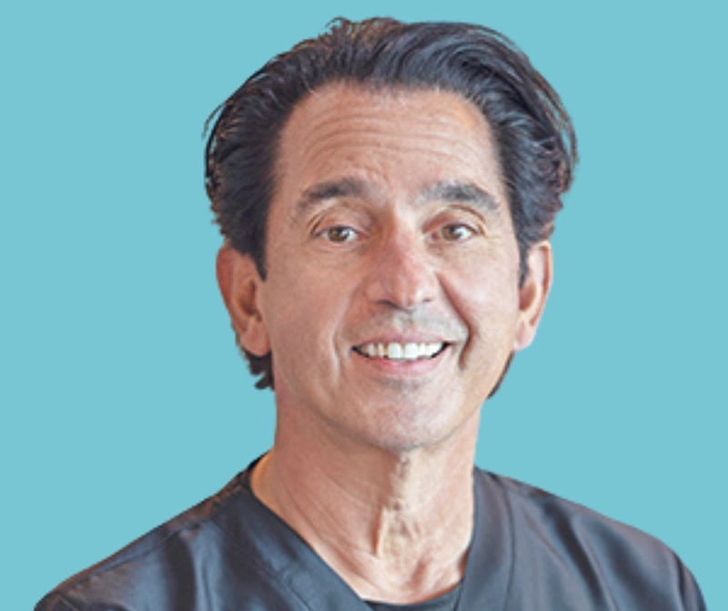 Smiling male dental professional against blue background for dental practice website.