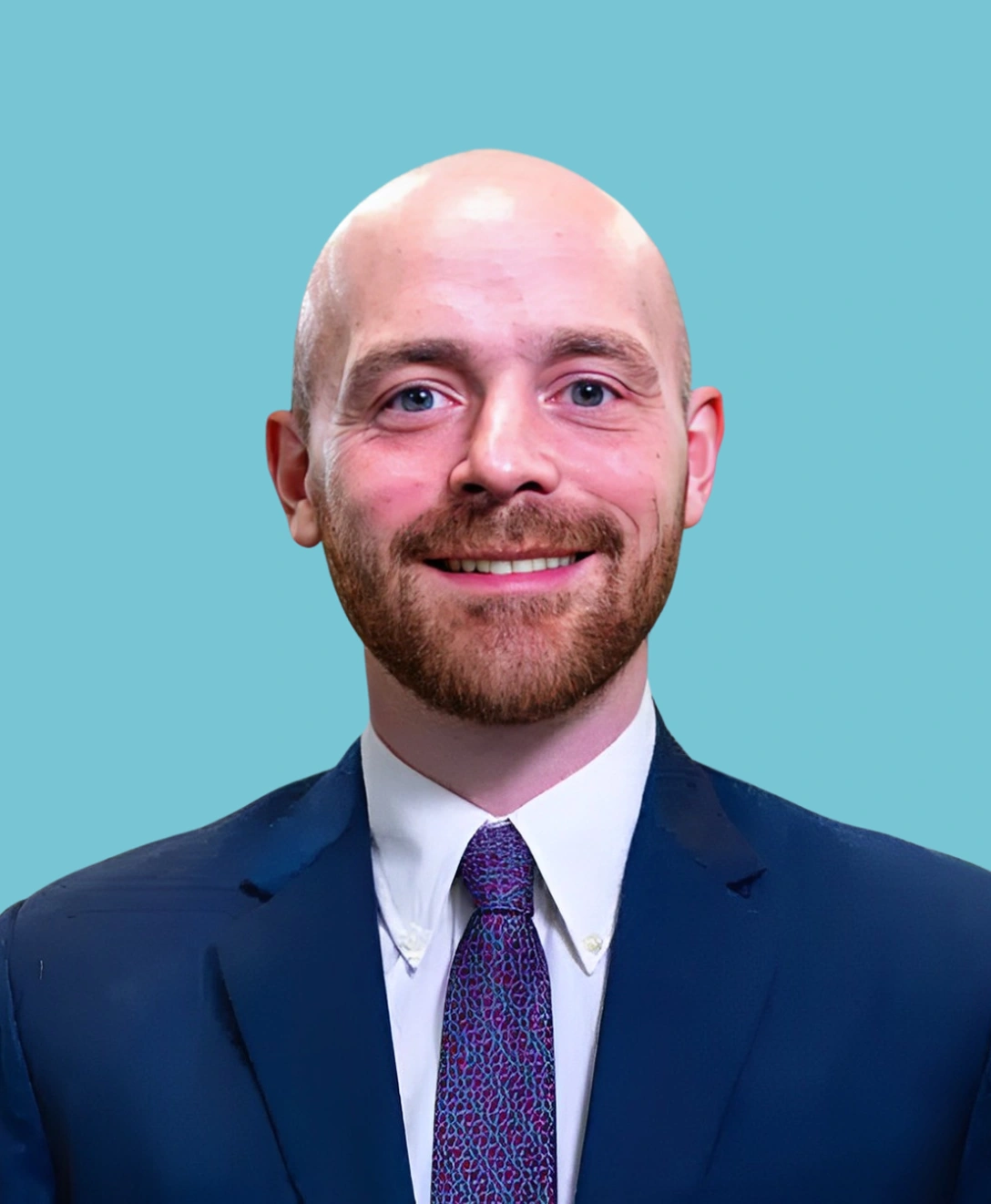 Professional headshot of bald man with beard wearing navy suit and purple tie against blue background.